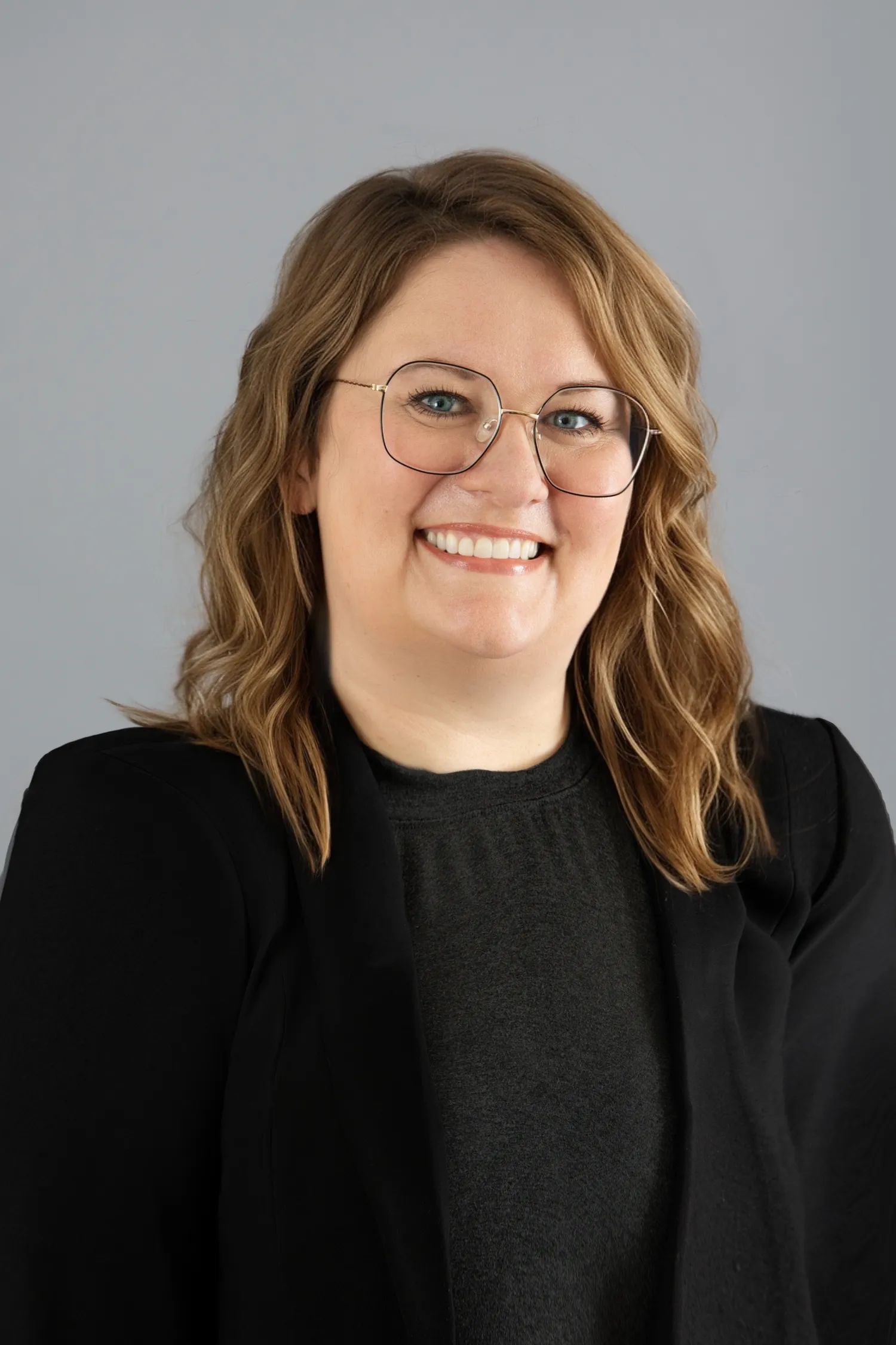 Professional headshot of a woman with glasses wearing a black blazer