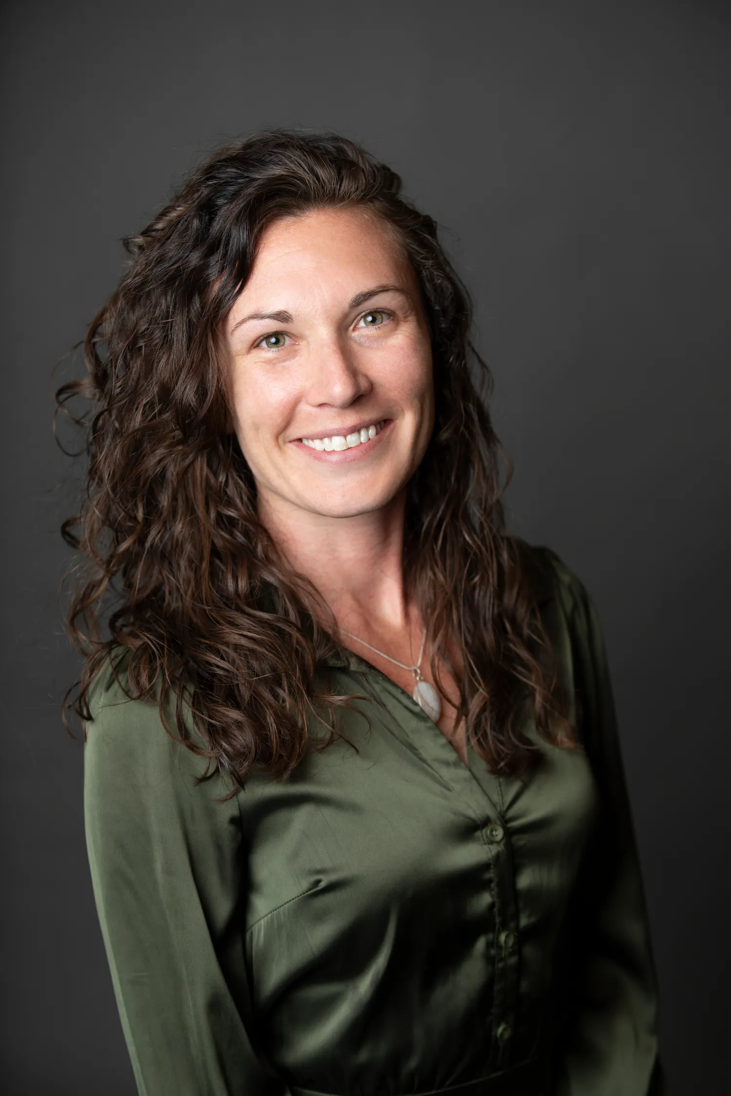 Professional headshot of a woman with curly brown hair wearing a green blouse