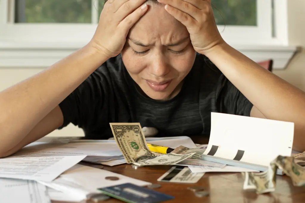 Stressed person reviewing bills and money at table
