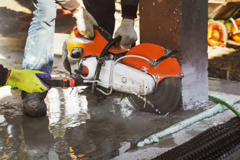 Gloved worker operates water sprayer over industrial cleaning machine