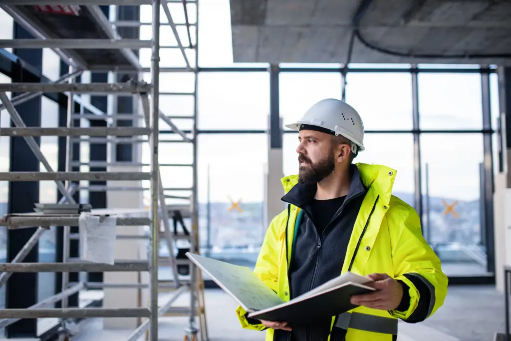 Construction worker reviews plans beside metal scaffolding