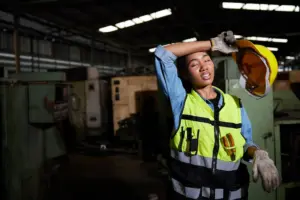 Factory worker removes hard hat, wiping sweat in workshop